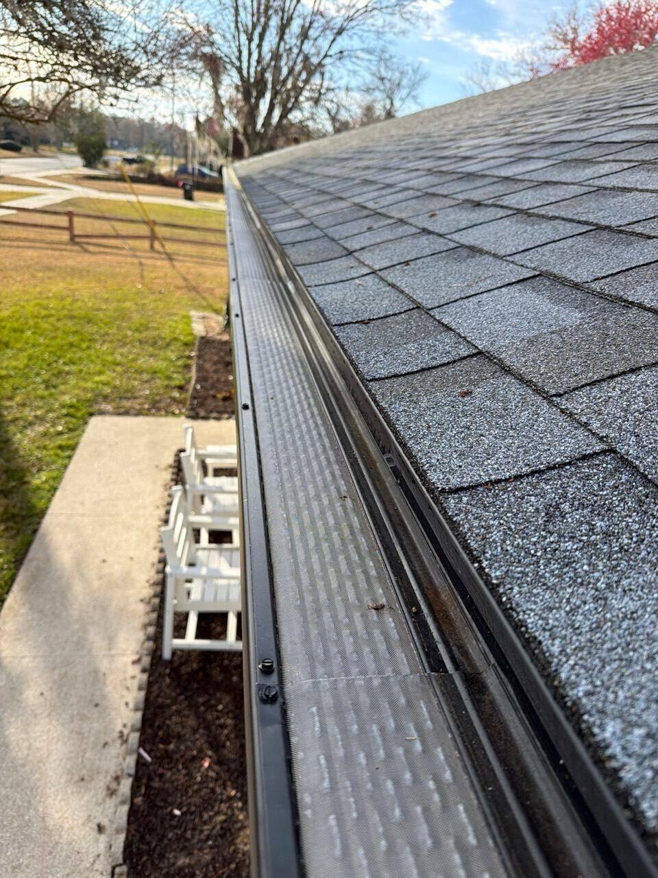 Close view of a black micro-mesh gutter guard installed along a shingle roof